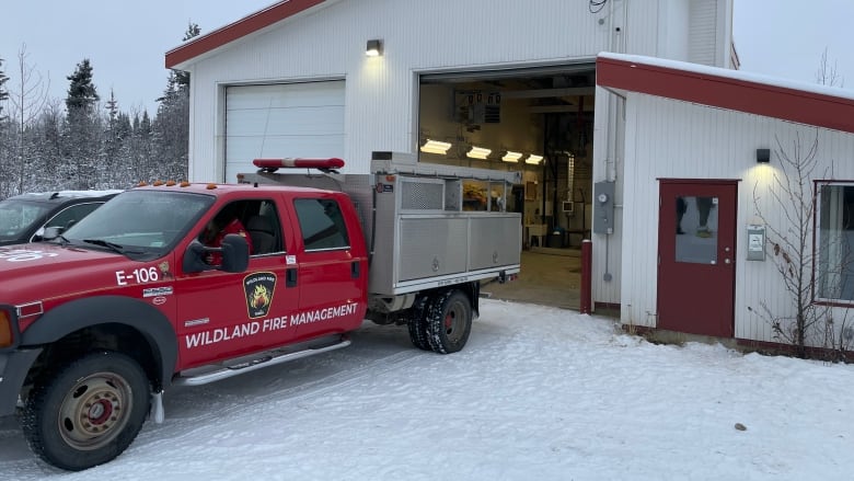 A red pickup truck labelled 'wildland fire management' sits on a snowy driveway outside a garage.