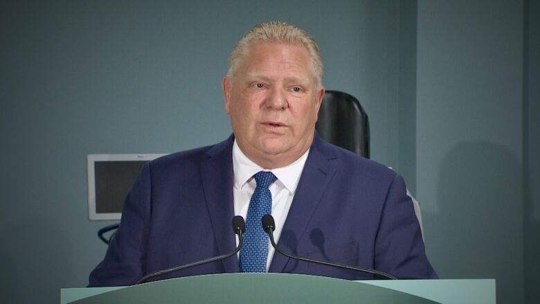 Ontario Premier Doug Ford speaks at a podium, wearing a blue suit and tie.