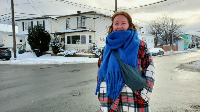 A woman with a red coat and blue scarf standing in front of a white building. 