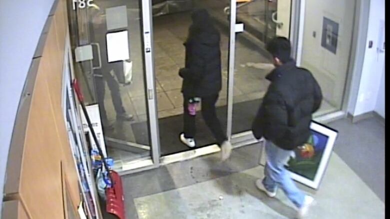 A woman and man are pictured exiting the lobby of a building, the man holding a colorful painting. 