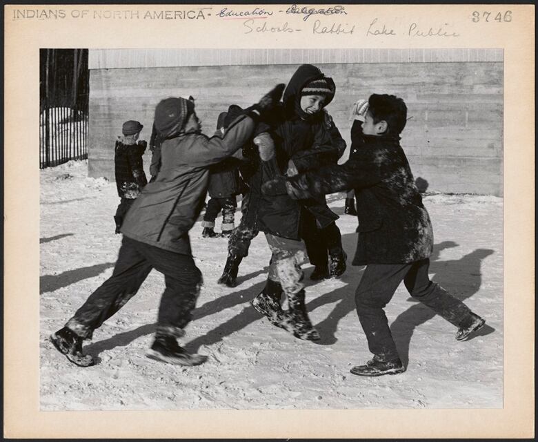 Three children play, pushing each other and smiling in the snow.