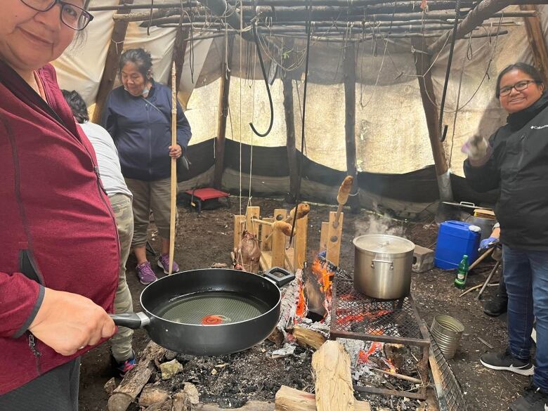 A group of Indigenous women cook traditional food, including goose, moose and bannock over an open fire in a hard walled teepee in Kahnawake, Que.