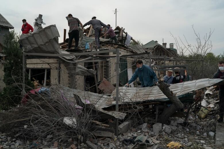 People standing on top of a destroyed home, moving debris.