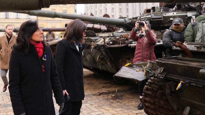 A woman in a black jacket and red scarf walks by a row of tanks