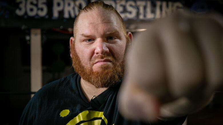 A man with a red beard and short hair scowls and holds his fist toward the camera.