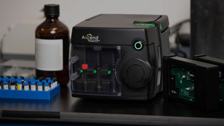 An up-close picture of a black box with knobs and buttons on it, next to a drug bottle and vials.