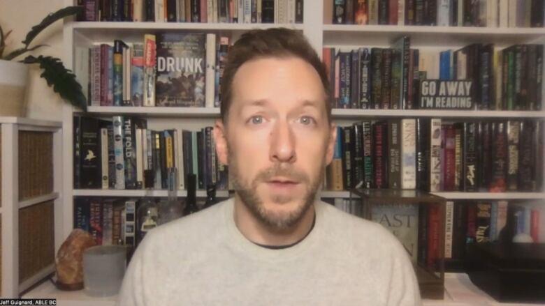 A man sits in front of a bookshelf