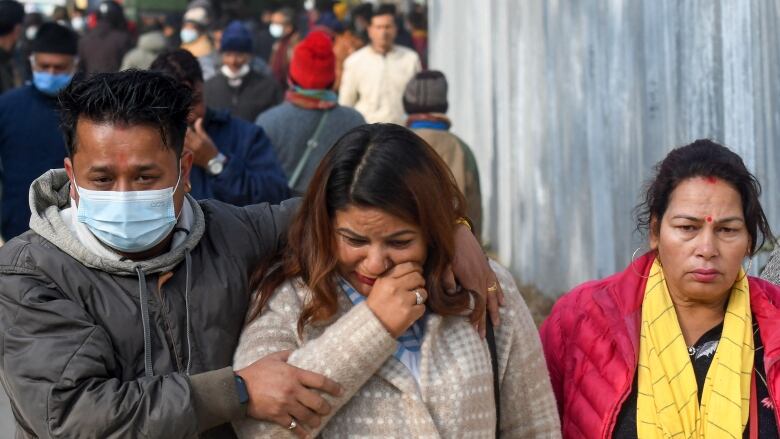 Two women and a men appear forlorn, with one woman appearing to wipe a tear from her face.