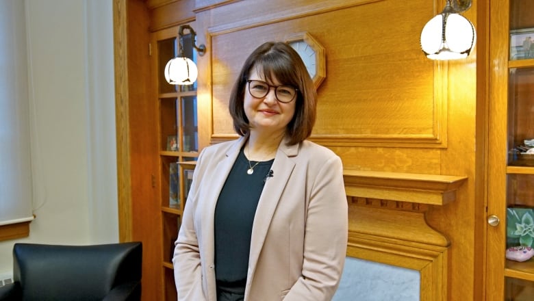 A woman with glasses stands in front of a fireplace in an office.