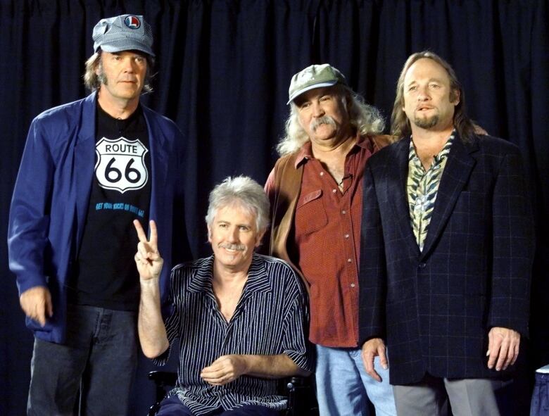 Four men pose for a photo. Three men are standing and one is sitting and giving a peace sign.