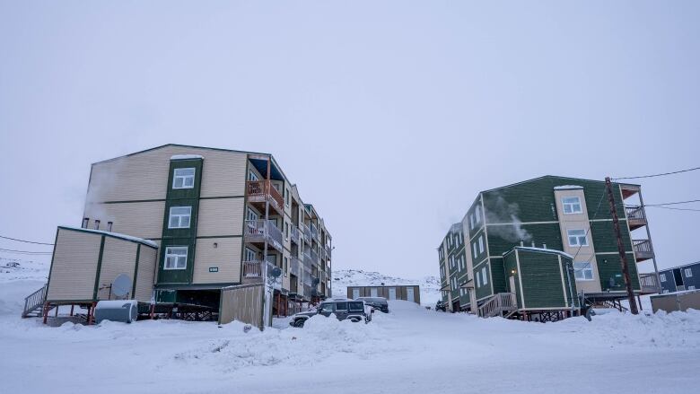 Two three-storey apartment buildings on stilts in snow. 