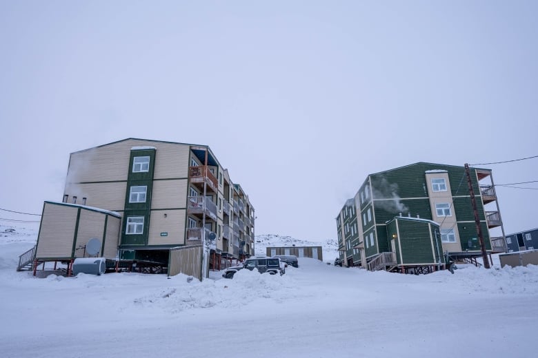 Two three-storey apartment buildings on stilts in snow. 