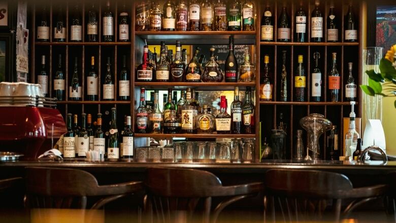 A wall shelf full of wine and liquor bottles is pictured behind a bar.