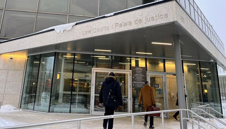 A person in a black winter coat and another in a brown coat enter a building with the words Law Courts inscribed above a set of doors.