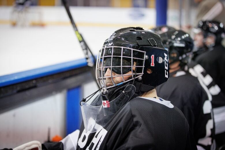 A goaltender sitting on the bench wears an eye mask under his goalie mask.