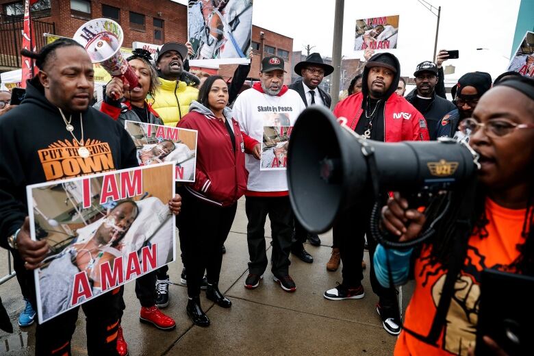 Protesters hold signs and megaphones while standing on a sidewalk. 