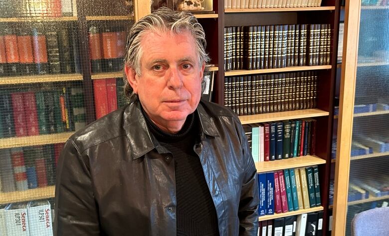 A man in a leather jacket poses in front of a bookcase.