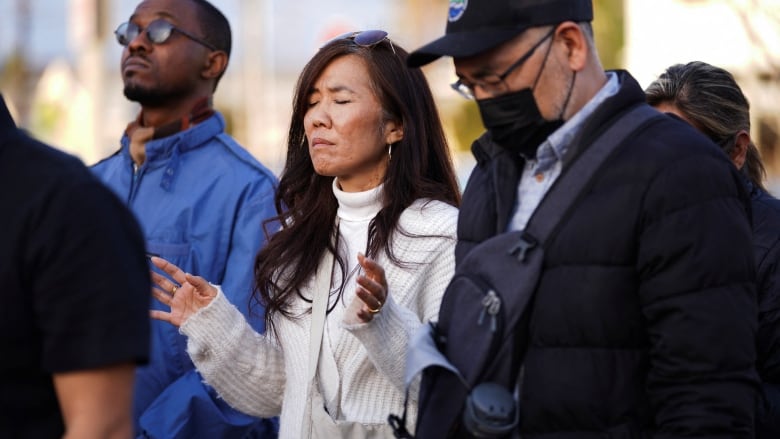 A woman and two men stand with eyes closed.