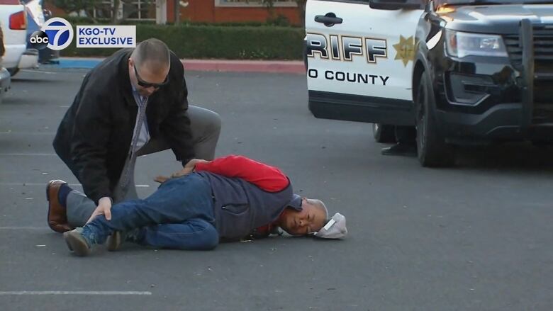 A man lying on the ground being subdued by a law enforcement agent.