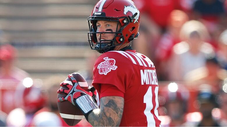 Men's quarterback wearing a Stampeders uniform, prepares to throw the ball during a CFL game.