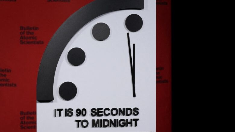 An oversized clock shows the hour hand near midnight, with the minute hand placed at 90 seconds to midnight.