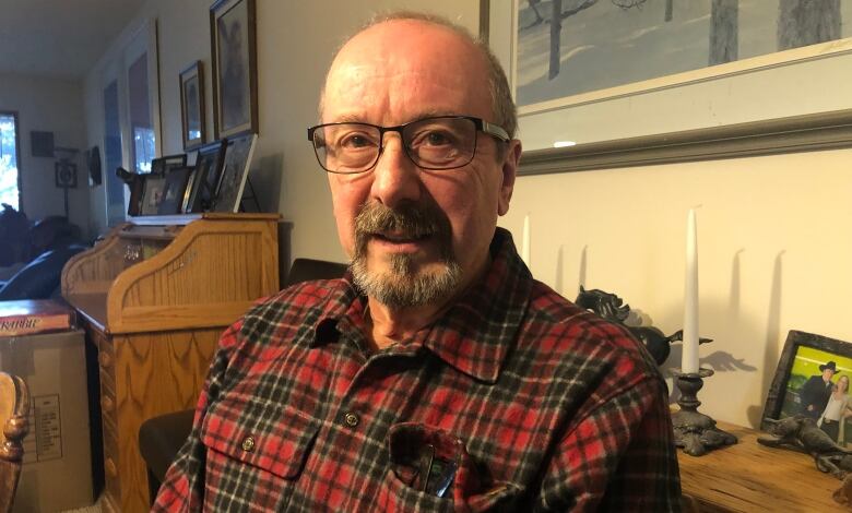 A man sits at a dining room table. He's wearing a red plaid shirt. 