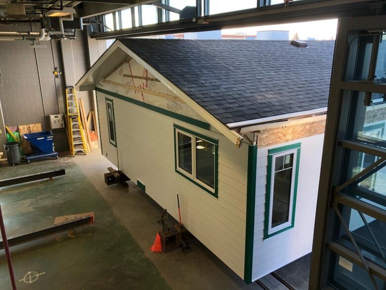 A white home with a green roof is being moved out of a hangar space.