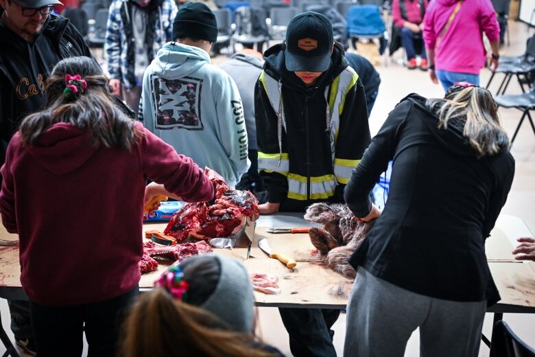 Teenagers leaning on a table covered in cardboard, carcasses.