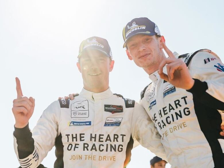 Two racing drivers wearing Michelin caps holding up their index fingers