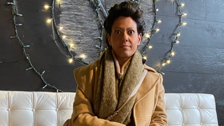 Natalie sits in front of a wall of lights on a white leather sofa