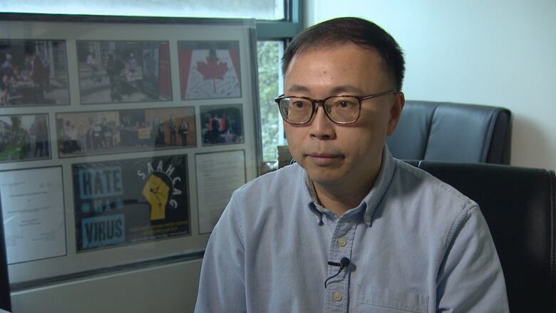 Ivan Pak looking being interviewed in his office, wearing glasses and a blue button up shirt.