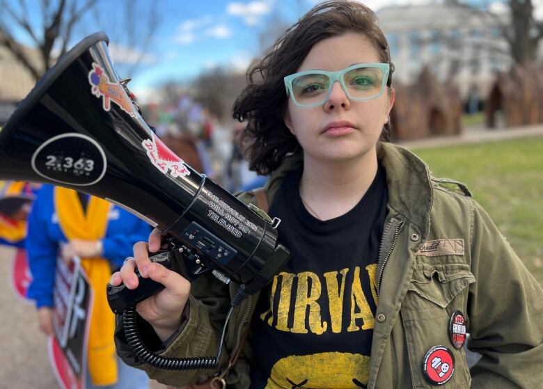 A young woman wearing green-rimmed glasses holds a black bullhorn.