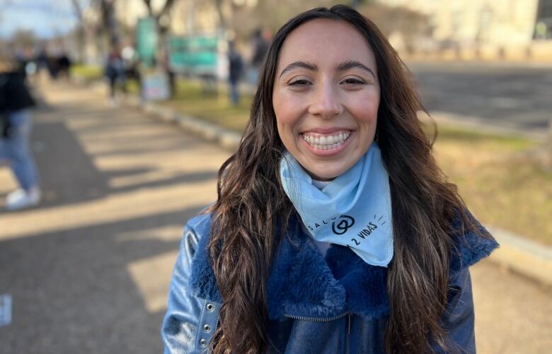 A young woman with long brown hair and wearing a blue jacket smiles at the camera.