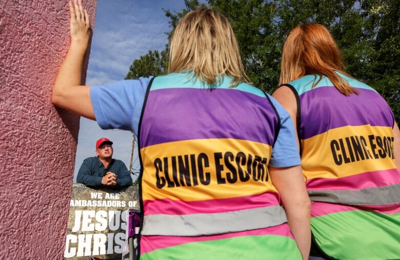 Two women wearing brightly coloured vests that say 