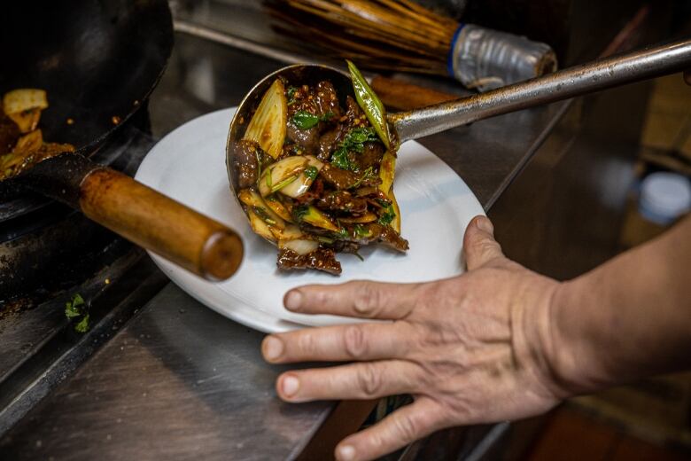 A large spoonful of cumin beef being plated at Wong's Asian Cuisine.