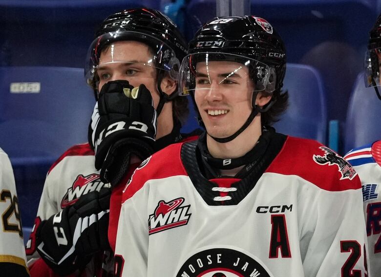 Three hockey players in three different junior hockey team jerseys stand on the ice during a practice.