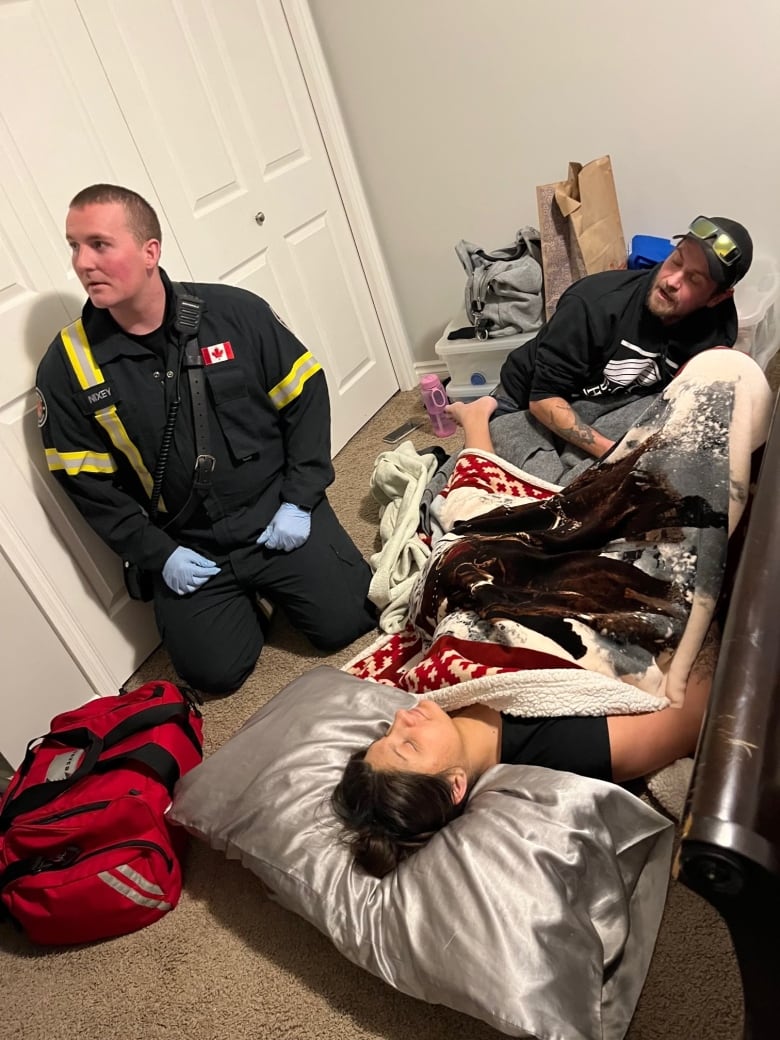 A woman lies on a floor next to a firefighter and another man.