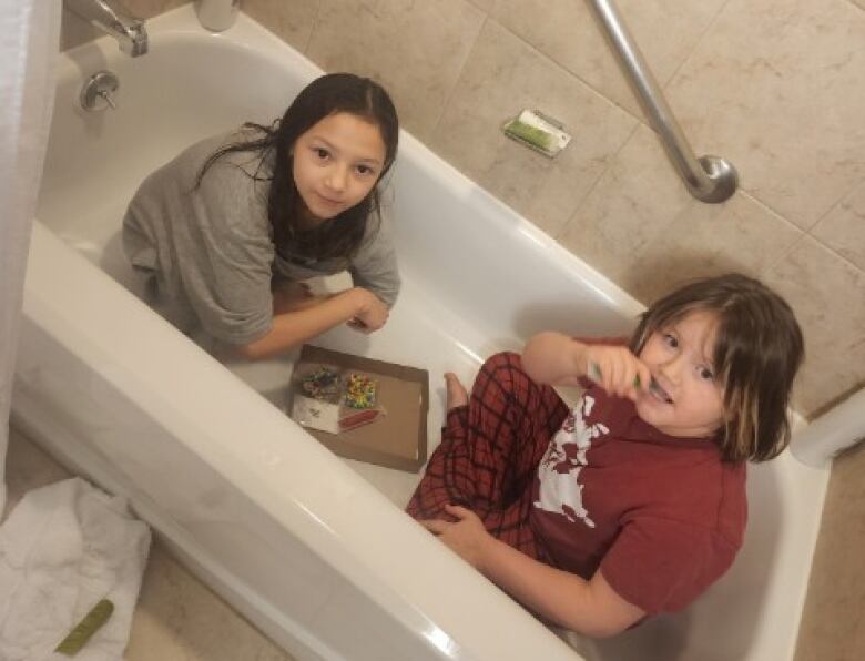 Two children, fully clothed, playing a board game in an empty bathtub.