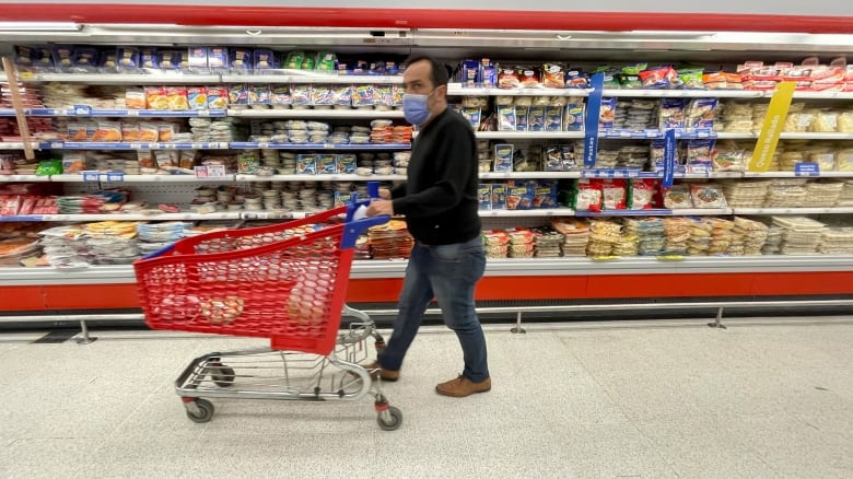 A masked man walks by a refrigerated section of a grocery store.