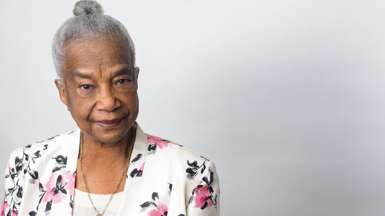 A head and shoulders shot of an older Black woman with greying hair tucked in a neat bun, wearing a floral jacket.