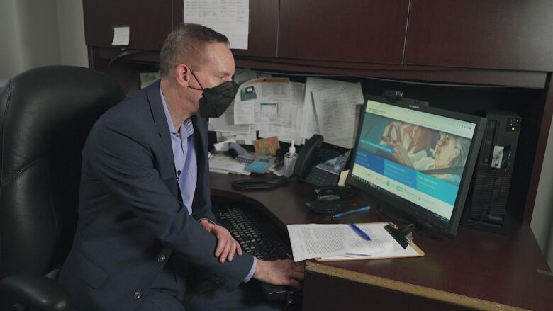 A man wearing a mask sits in front of a computer.