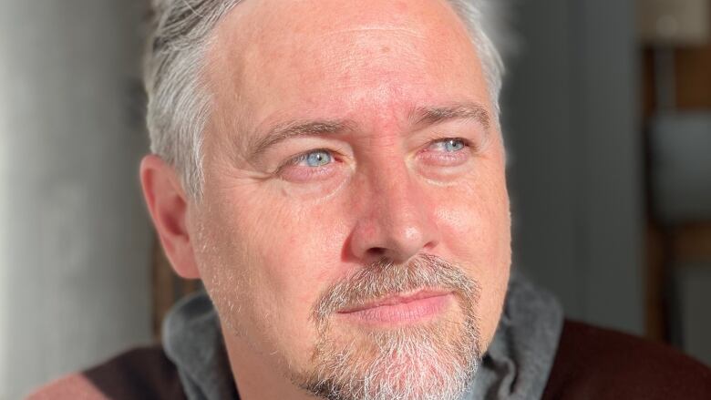 A man with greying hair and blue eyes looks into the distance