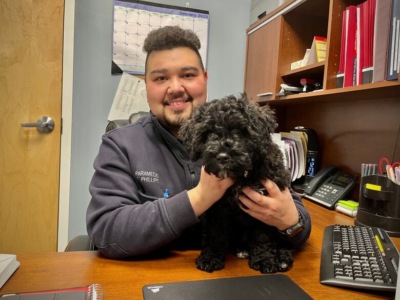 Tanner Phillips, a paramedic and the Quality Assurance and Medical Instructor, holds the new puppy at his desk.