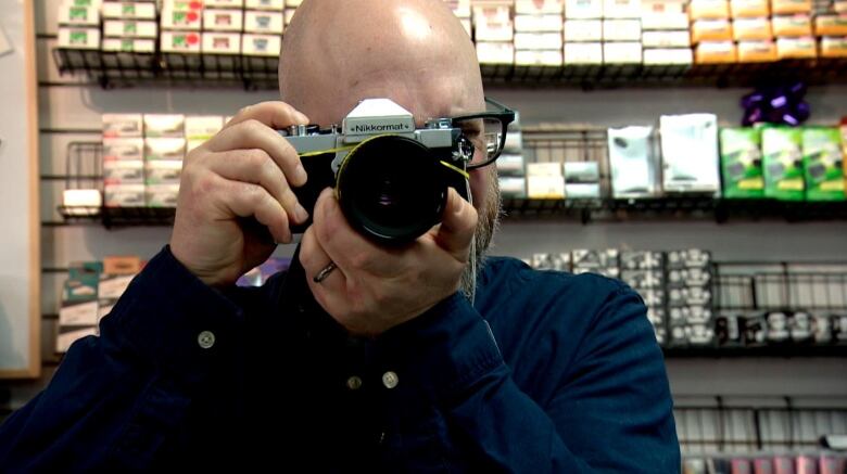 A camera store owner takes a photo with a film camera.