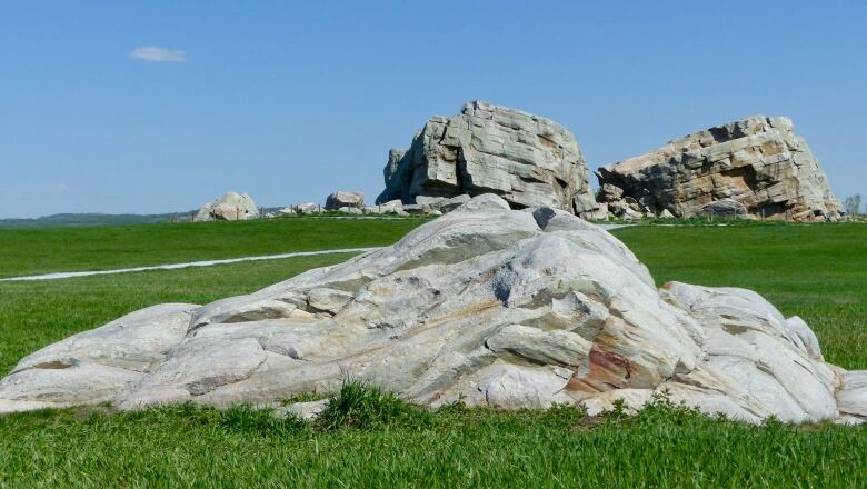 Blue signs describing the history of the rock sit on sidewalks, with the massive Okotoks erratic in the distance.