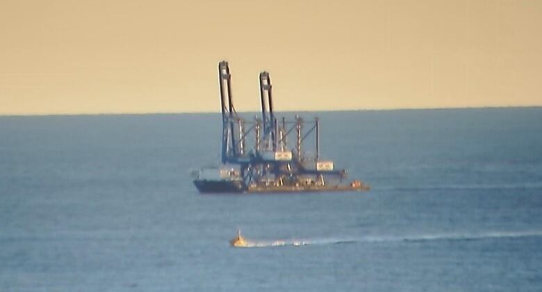 A boat in the distance carrying two big cranes. 