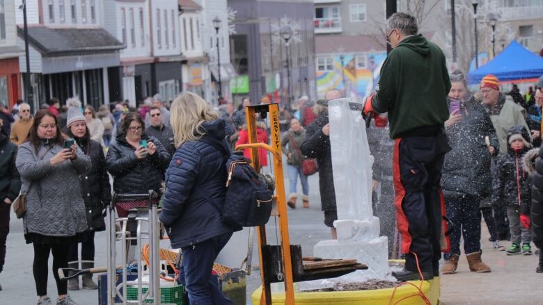 A man sculpts and ice sculpture while people watch and take photos