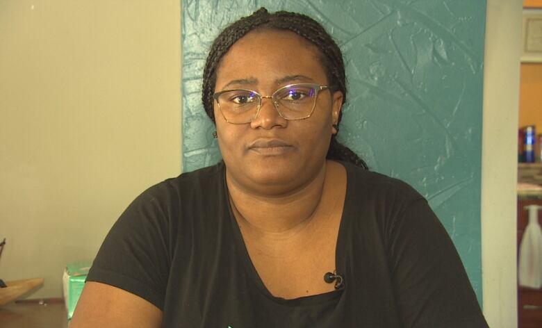 A woman with braided hair and glasses stares solemnly at the camera.