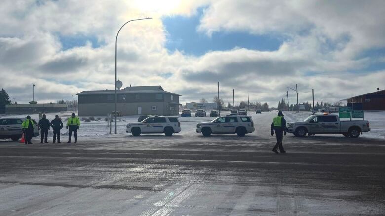 Police officers stand in front of parked police cars on a highway road.