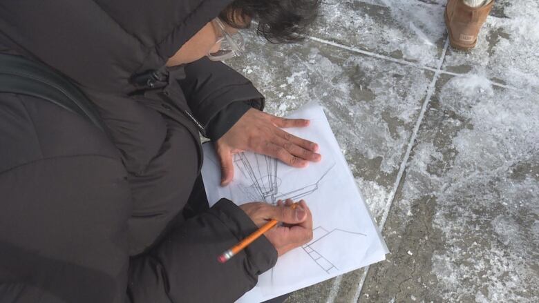 A man wearing a black jacket kneeled down while drawing on a piece of blank paper.